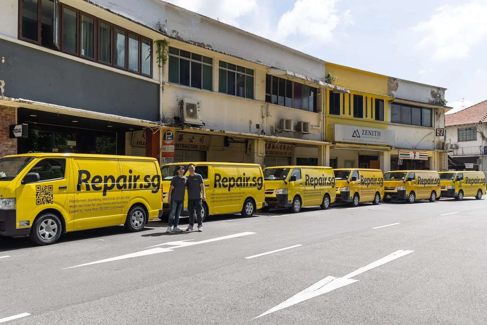 A row of yellow Repair.sg vans on a shophouse street, two of the team standing in front